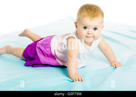 Babymädchen in einem Kleid kriecht auf die blaue Tagesdecke Stockfoto