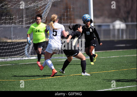 Ein Verteidiger führt eine Kopfzeile, um die Kugel von der vor ihr Keeper und Ziel Mund während einer High School Fußballspiel zu löschen. USA. Stockfoto