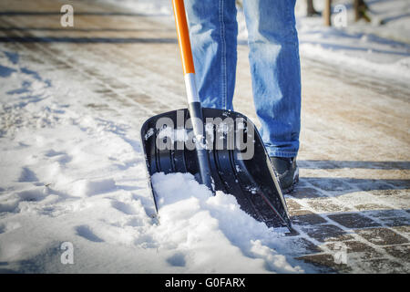 Mann mit Schneeschaufel reinigt Gehwege im winter Stockfoto