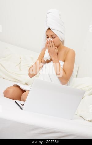 Junge Frau in ihrem Bett sitzen und ihre Nase weht Stockfoto