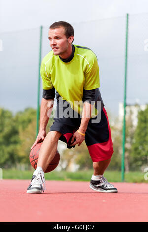 Junger Mann am Basketballplatz mit Ball dribbeln. Streetball Stockfoto