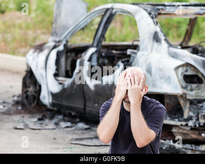 Weint aufgeregt Mann auf Brandstiftung Feuer verbrannten Auto Fahrzeug Stockfoto