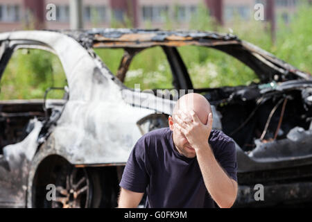 Weint aufgeregt Mann auf Brandstiftung Feuer verbrannten Auto Fahrzeug Stockfoto