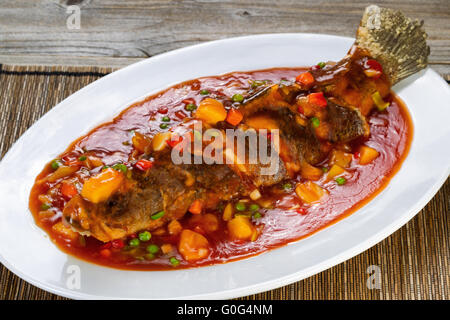 Gebratener ganzer Fisch in Sauce mit Obst und Gemüse in weiß Teller bereit, Essen Stockfoto
