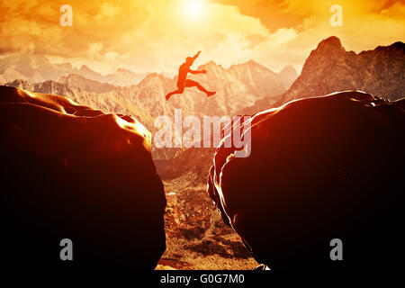 Mann springt über den Abgrund zwischen zwei felsigen Berge bei Sonnenuntergang. Freiheit Stockfoto