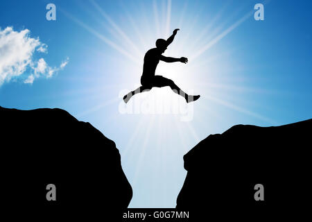 Mann springt über den Abgrund zwischen zwei felsigen Bergen im Sonnenlicht. Freiheit Stockfoto