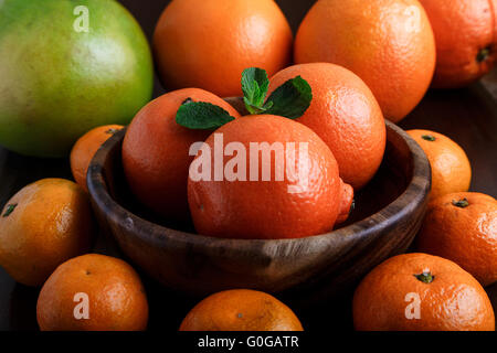 Mandarinen in Holzteller mit Mandarinen, Orangen und Minze Blätter auf dunklem Hintergrund Nahaufnahme Makro Stockfoto