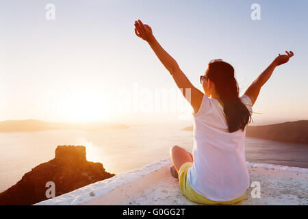 Junge Frau sitzt mit Händen und bewundert die Caldera-Aussicht auf Santorini Stockfoto