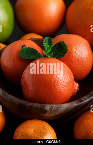 Mandarinen in Holzteller mit Mandarinen, Orangen und Minze Blätter auf dunklem Hintergrund Nahaufnahme Makro Stockfoto