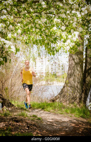 Ein senior Mann in schwarz und gelb getragen läuft in den Wald, am See, während ein warmer Frühlingstag Stockfoto