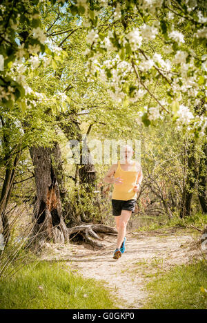Ein senior Mann in schwarz und gelb getragen läuft im Wald, am See, unter einer Apfelblüte im warmen Frühling Stockfoto