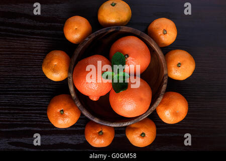 Mandarinen in Holzteller mit Mandarinen und Minze Blätter auf dunklem Hintergrund Nahaufnahme Makro Stockfoto