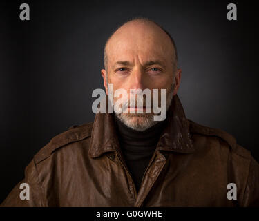 ernste und konzentrierte senior woman in Lederjacke - ein Kopfschuss vor schwarzem Hintergrund Stockfoto