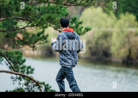 junge Sportler Mann unterwegs im Frühling Park läuft. Anhören von Musik über Kopfhörer Stockfoto