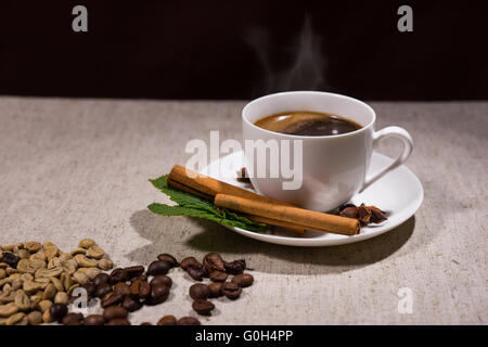 Heißen Kaffee in weiß Elfenbein farbigen Tasse mit Zimtstangen und Bohnen über graue Tischdecke mit schwarzem Hintergrund Stockfoto