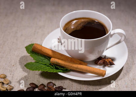 Heißen Kaffee in weiß Elfenbein farbigen Tasse mit Zimtstangen und Bohnen über graue Tischdecke mit schwarzem Hintergrund Stockfoto