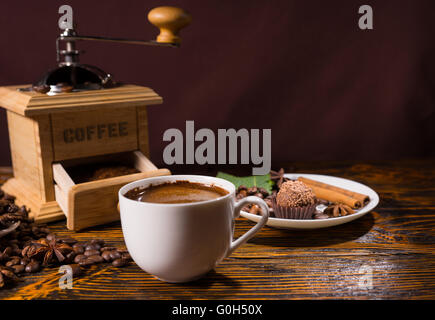 Tasse heißes Getränk neben Schokoladendessert mit Zimtstangen und Sternanis in der Nähe von offenen Kaffeemühle Stockfoto