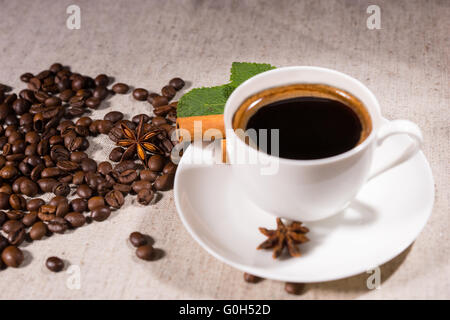 Frische schwarze Kaffee im Becher auf weißen Teller von Sternanis und losen Bohnen auf natürliche getönten Leinwand Stockfoto