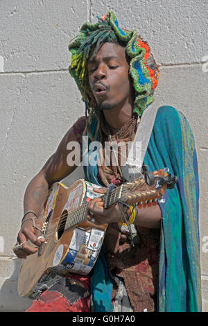 Ein Straßenmusikant in einem bunten Hut & Outfit spielen & singen auf der Gitarre im Washington Square Park in New York City Stockfoto