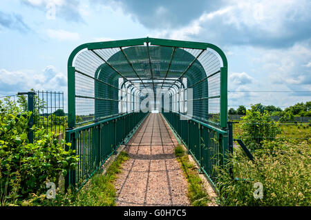 Ein rosa Kiesweg führt zu einer Fußgängerbrücke über die Autobahn M6 Toll, Chasewater Country Park durch grüne Sicherheit Netz geschützt * Stockfoto