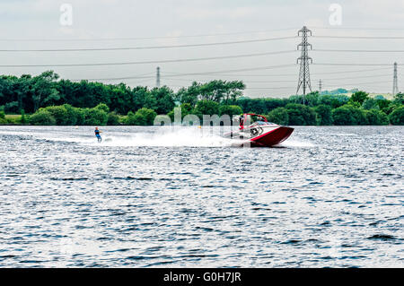 An einem Nachmittag der grauen Feder gleitet ein Motorboot über die abgehackt Oberfläche des Chasewater Stausees Abschleppen eines Wasserschifahrer in seinem Gefolge Stockfoto