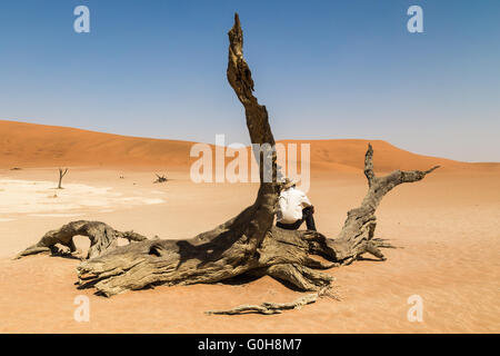 Einsamer Mann sitzt auf einem Baumstumpf in der Mitte der namibischen Wüste. Gedanken über Natur, tolle Aussichten. Stockfoto