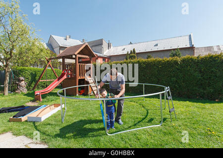 Vater und Sohn bei der Installation von großen Garten Trampoline. Bau von privaten Spielplatz. der Arbeitnehmer und sein kleiner Helfer. Stockfoto