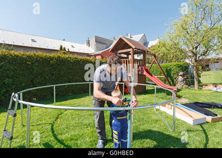 Vater und Sohn bei der Installation von großen Garten Trampoline. Bau von privaten Spielplatz. Der Arbeiter und seine kleinen Helfer. Stockfoto