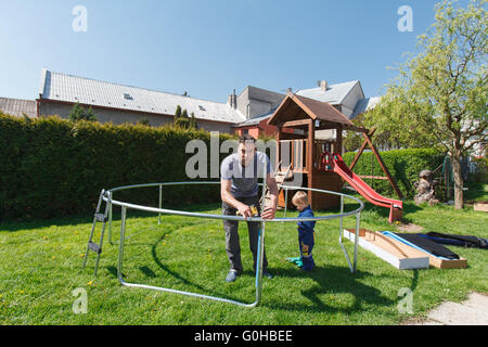 Vater und Sohn bei der Installation von großen Garten Trampoline. Bau von privaten Spielplatz. Der Arbeiter und seine kleinen Helfer. Stockfoto