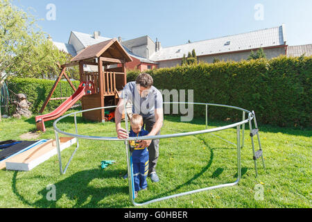 Vater und Sohn bei der Installation von großen Garten Trampoline. Bau von privaten Spielplatz. der Arbeitnehmer und sein kleiner Helfer. Stockfoto