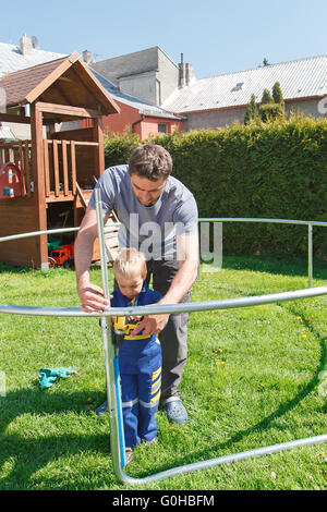 Vater und Sohn bei der Installation von großen Garten Trampoline. Bau von privaten Spielplatz. Der Arbeiter und seine kleinen Helfer. Stockfoto