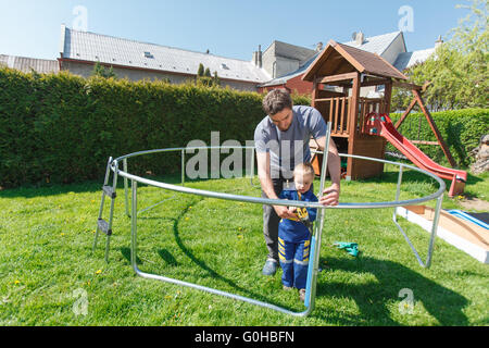 Vater und Sohn bei der Installation von großen Garten Trampoline. Bau von privaten Spielplatz. Der Arbeiter und seine kleinen Helfer. Stockfoto