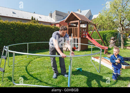 Vater und Sohn bei der Installation von großen Garten Trampoline. Bau von privaten Spielplatz. der Arbeitnehmer und sein kleiner Helfer. Stockfoto