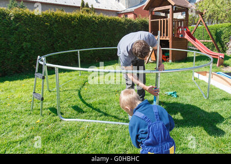 Vater und Sohn bei der Installation von großen Garten Trampoline. Bau von privaten Spielplatz. Der Arbeiter und seine kleinen Helfer. Stockfoto