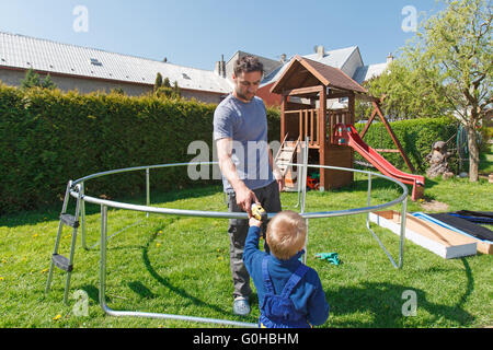 Vater und Sohn bei der Installation von großen Garten Trampoline. Bau von privaten Spielplatz. der Arbeitnehmer und sein kleiner Helfer. Stockfoto