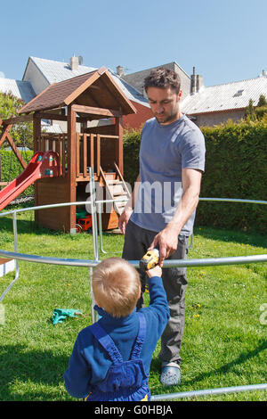 Vater und Sohn bei der Installation von großen Garten Trampoline. Bau von privaten Spielplatz. der Arbeitnehmer und sein kleiner Helfer. Stockfoto