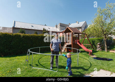 Vater und Sohn bei der Installation von großen Garten Trampoline. Bau von privaten Spielplatz. Der Arbeiter und seine kleinen Helfer. Stockfoto