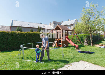 Vater und Sohn bei der Installation von großen Garten Trampoline. Bau von privaten Spielplatz. Der Arbeiter und seine kleinen Helfer. Stockfoto