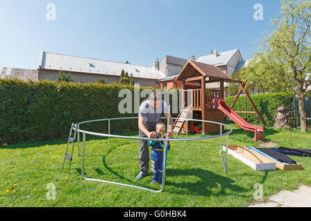 Vater und Sohn bei der Installation von großen Garten Trampoline. Bau von privaten Spielplatz. der Arbeitnehmer und sein kleiner Helfer. Stockfoto