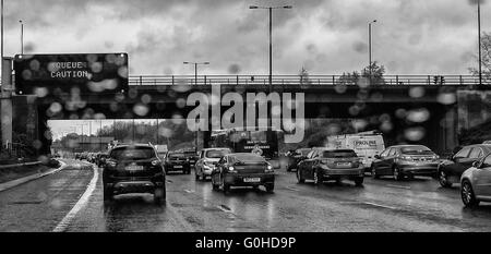 Queuing Verkehr auf Autobahn mit Overhead matrix Schild Warteschlange Vorsicht leicht durch Regentropfen auf der Windschutzscheibe verschwommen Stockfoto