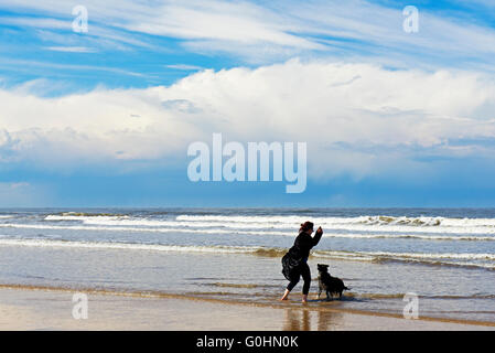 Frau wirft einen Stick für ihren Hund am Strand von Holkham, Norfolk, England UK Stockfoto