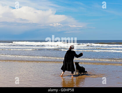 Frau wirft einen Stick für ihren Hund am Strand von Holkham, Norfolk, England UK Stockfoto