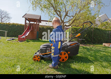 Süßen, kleinen Jungen mäht den Rasen. Junge inspiziert den Mäher vor treibende oder links Motoröl. Stockfoto