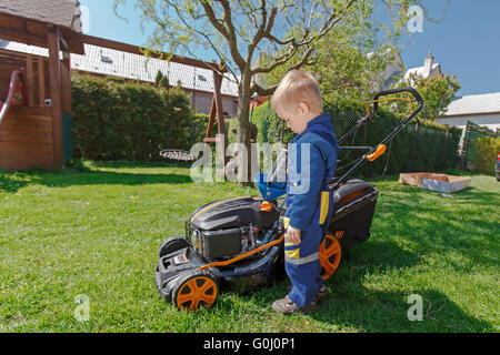 Süße, kleine Junge mäht den Rasen. Junge inspiziert die Mäher, bevor sie Auto fahren oder Links Motoröl. Stockfoto