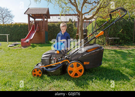 Süßen, kleinen Jungen mäht den Rasen. Junge inspiziert den Mäher vor treibende oder links Motoröl. Stockfoto