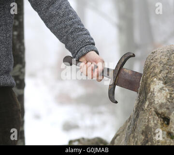 Hand des tapferen Ritters versucht, das magische Schwert Excalibur in den Stein zu entfernen Stockfoto