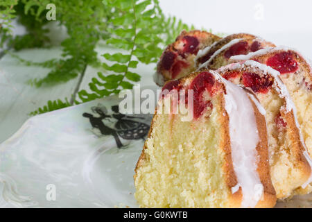 Nahaufnahme der Scheiben von glasierten Kirschen Kuchen auf Vintage weißen Teller mit Boston Farn auf Holztisch Stockfoto