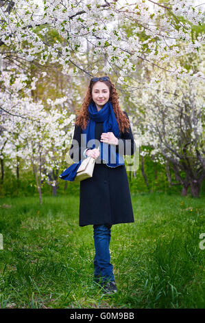 junge Frau im Mantel zu Fuß in der blühenden Kirschbaum Frühlingsgarten Stockfoto