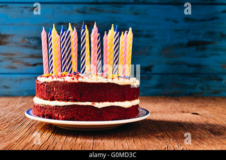 ein roter Samt-Kuchen, garniert mit einigen unbeleuchteten Kerzen auf einem rustikalen Holztisch Stockfoto