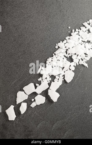 Draufsicht der Magnesium-Chlorid Flocken auf einem dunklen Granit Schiefer. Stockfoto